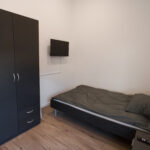 Kleines Schlafzimmer mit Einzelbett, dunklem Kleiderschrank und Wandfernseher.