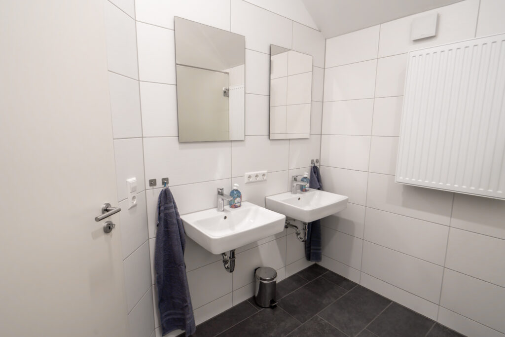 Badezimmer mit zwei Waschbecken, zwei Spiegeln, Handtüchern und Fliesenboden.