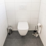 Modernes, weiß gefliestes WC mit wandhängender Toilette, Toilettenpapierhalter und