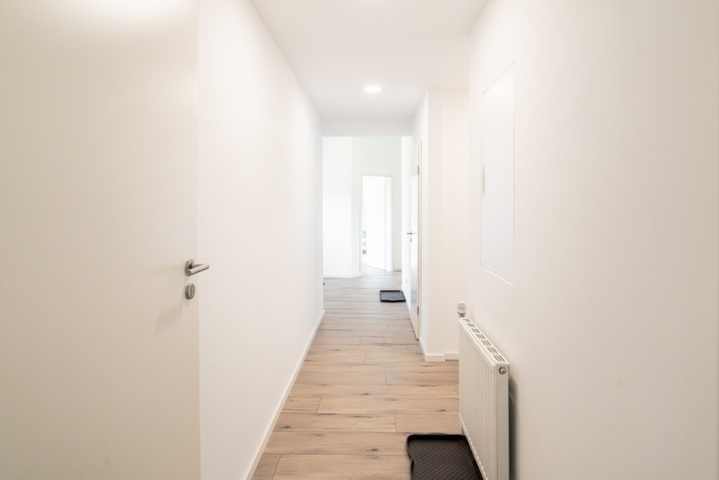Heller, langer Flur mit Holzfußboden, weißen Wänden und mehreren Türen.