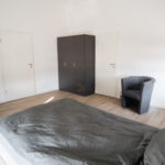 Modern eingerichtetes Schlafzimmer mit Doppelbett, dunklem Kleiderschrank und Fernseher.