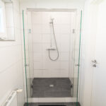 Begehbare Dusche mit Glaswänden und dunklem Fliesenboden in einem hell gefliesten Badezimmer.