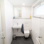 Modernes Badezimmer mit Hänge-WC, Waschbecken, Spiegel und Fenster.