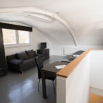 Wohnbereich unter dem Dach mit Sofa, Kleiderschrank, Esstisch, Fernseher und Bett im Hintergrund.